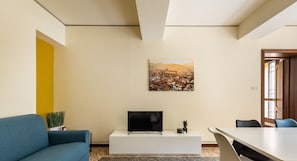 A modern living room with a flat-screen TV, a sofa, a dining table, and chairs.