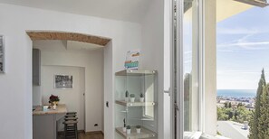 A small, bright room with a view of a cityscape, a wooden desk with a chair, and a shelving unit with plants. - Genova Wonderview by Wonderful Italy (Genova)