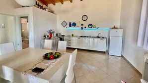 Una cocina moderna con electrodomésticos blancos, una zona de comedor con mesa dispuesta para dos personas y techo de madera.
