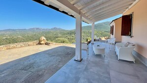 Un patio cubierto con mobiliario de mimbre blanco y vistas a colinas y montañas verdes.