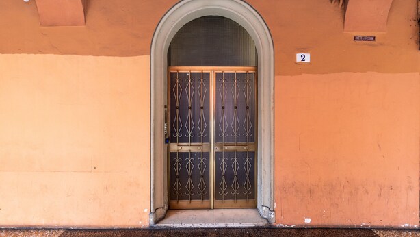 Entrada de um edifício com um grande arco, um portão de metal e uma pequena placa indicando o número 2.