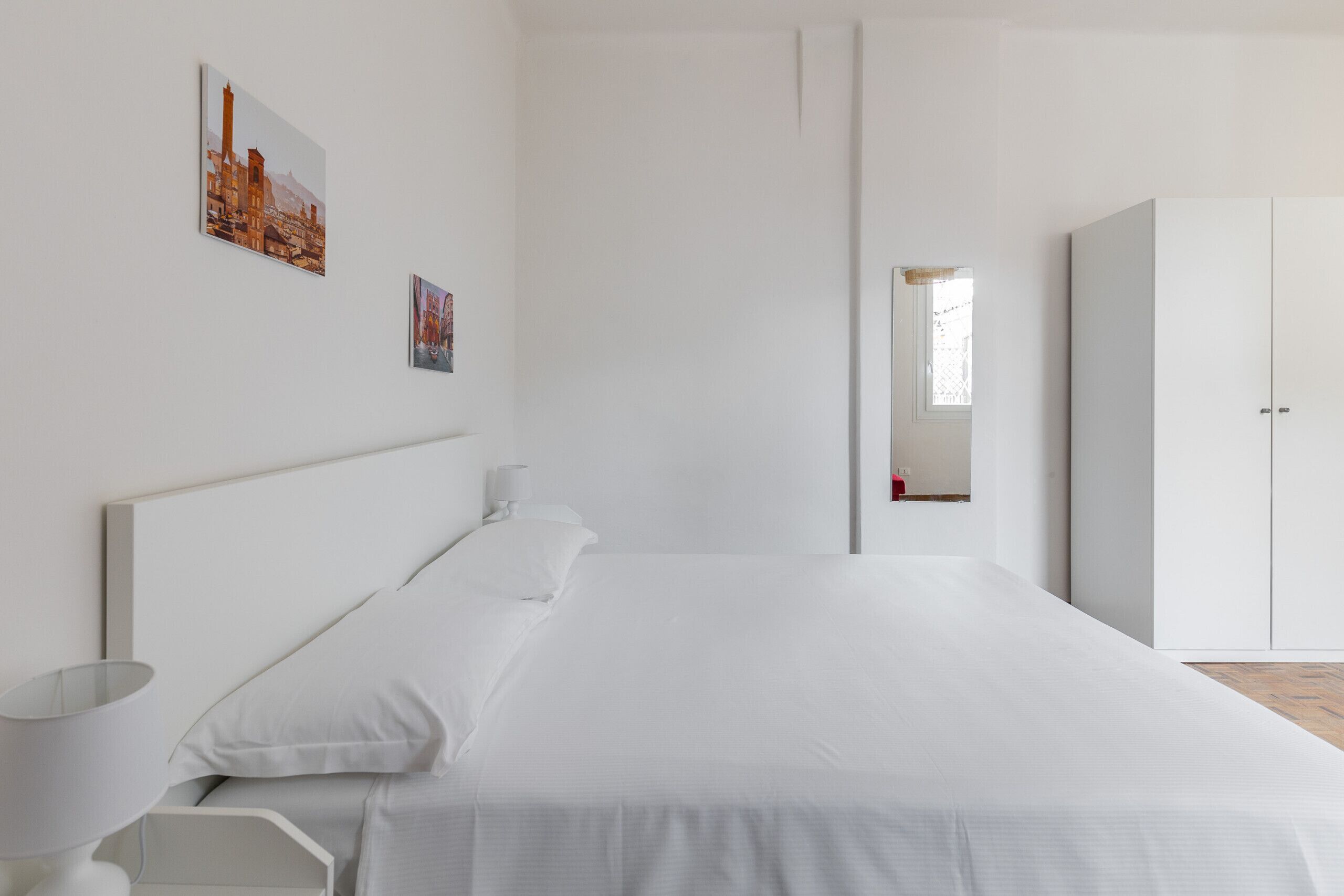 Une chambre à coucher au style minimaliste, avec un grand lit, une armoire et deux tableaux encadrés accrochés au mur.
