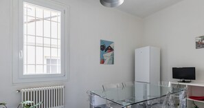 A modern office space with a glass table and chairs, a white radiator, a window, and a poster on the wall. - Appartamento alla Finestrella by Wonderful Italy (Bologna)
