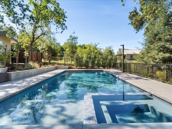 Una piscina rectangular con agua azul cristalina, rodeada por una plataforma de concreto y una cerca metálica.