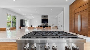 A modern kitchen with a stainless steel Wolf gas range, a large dining area with a glass-top table, and a stone fireplace. - Healdsburg Luxe Reserve for 8, pool, spa, firepit (Healdsburg)