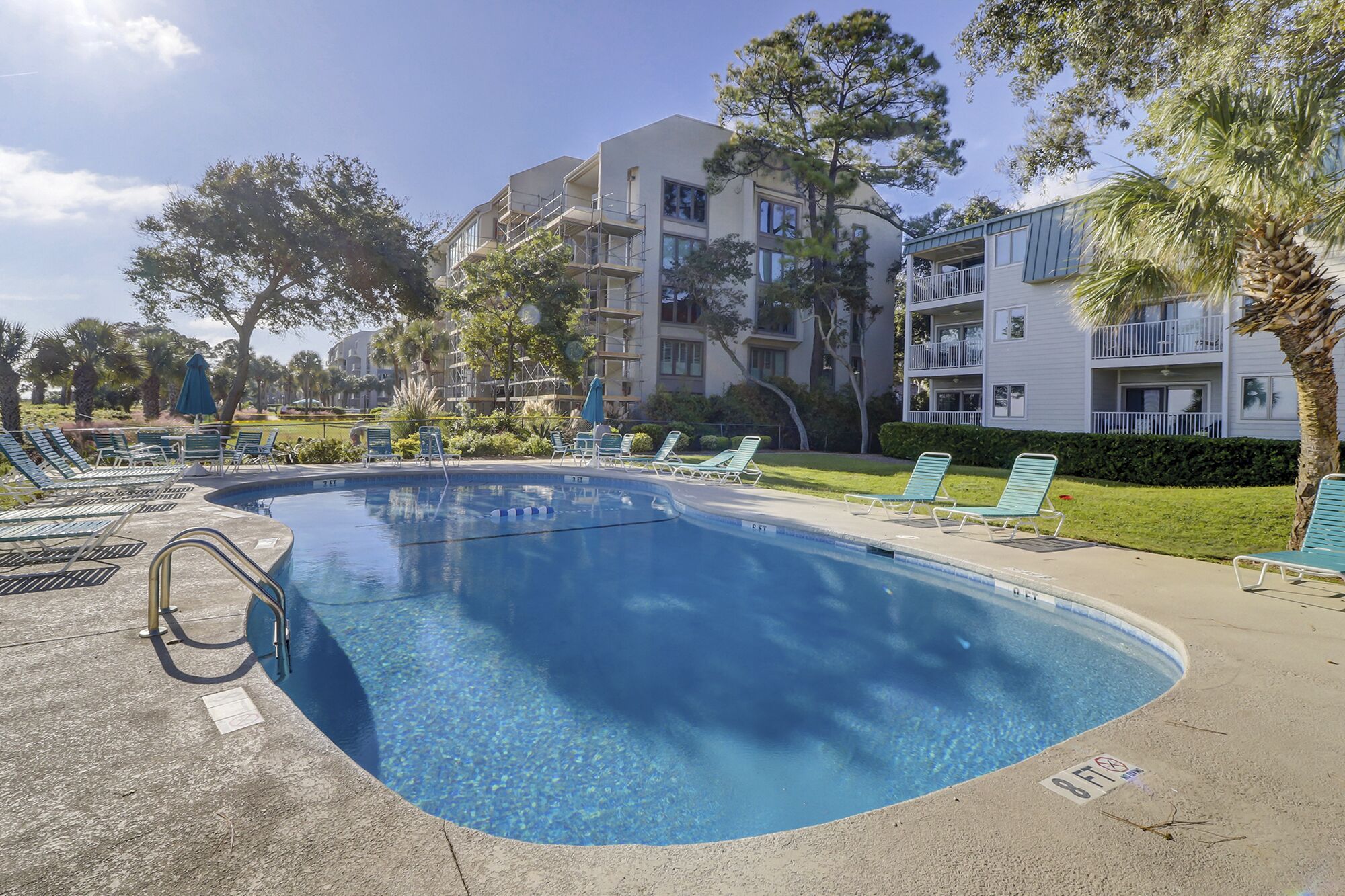 Une piscine dotée de chaises longues et d’un espace aménagé au bord de l’eau, le tout entouré d’immeubles à plusieurs étages dotés de balcons.