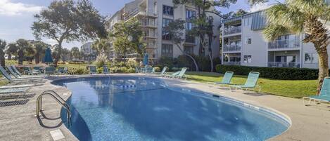 Une piscine dotée de chaises longues et d’un espace aménagé au bord de l’eau, le tout entouré d’immeubles à plusieurs étages dotés de balcons.