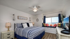 Ein Schlafzimmer mit einem Bett, Nachttischen, einem Deckenventilator, einem Fenster mit Vorhängen und einem Fernseher.