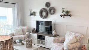 Ein Wohnzimmer mit Fernseher, Korbsessel, gestreifter Ohrensessel und Meerblick.