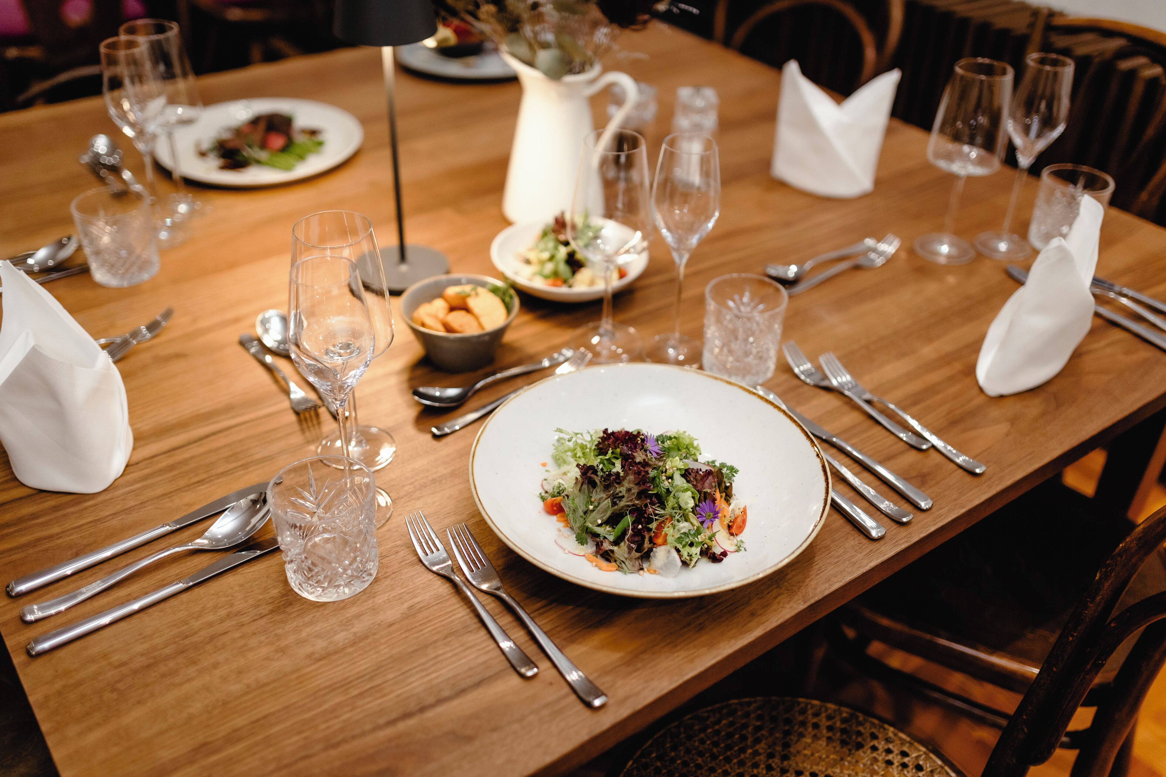 A dining table set for a meal with plates, cutlery, and glasses.