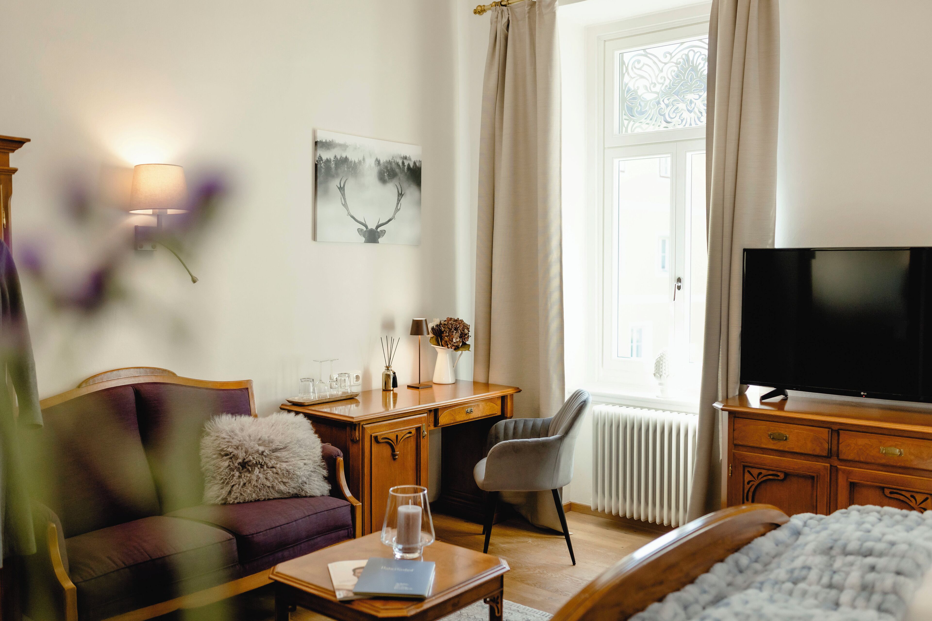 Een hotelkamer met een bed, een bureau met lamp, een televisie, een bank en een raam met gordijnen.