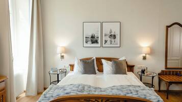 Un letto rifatto con cura, una testiera in legno, due comodini con lampade, un tavolino tondo con lampada e due quadri appesi al muro.