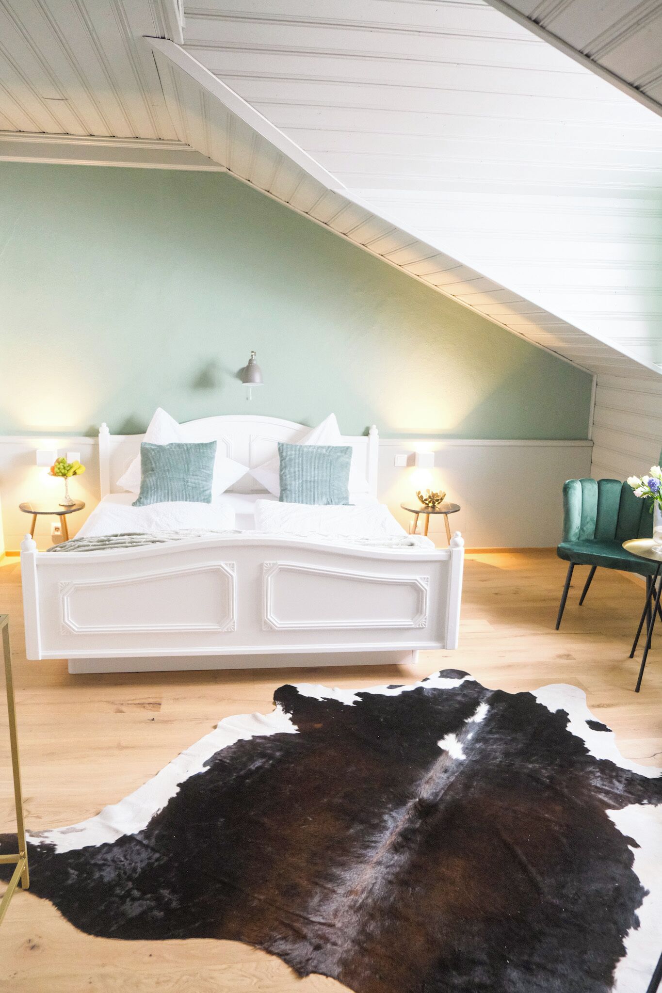 Una camera da letto con un letto bianco, cuscini verdi, un tappeto in pelle di vacca e una sedia verde.