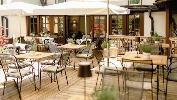 An outdoor café with multiple tables and chairs, large umbrellas, and potted plants. - Boutiquehotel Hubertushof (Bad Ischl)