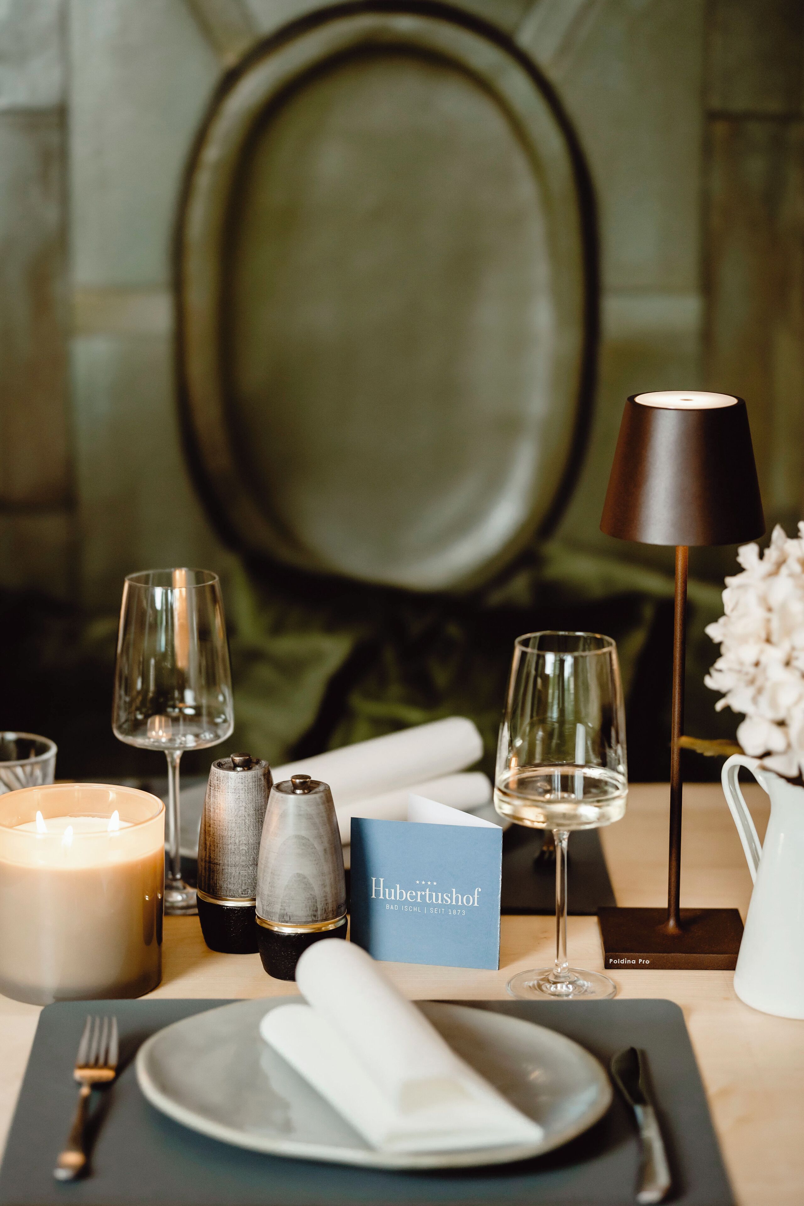 A table set with a candle, salt and pepper shakers, a folded napkin, a glass of water, a wine glass, and a menu.