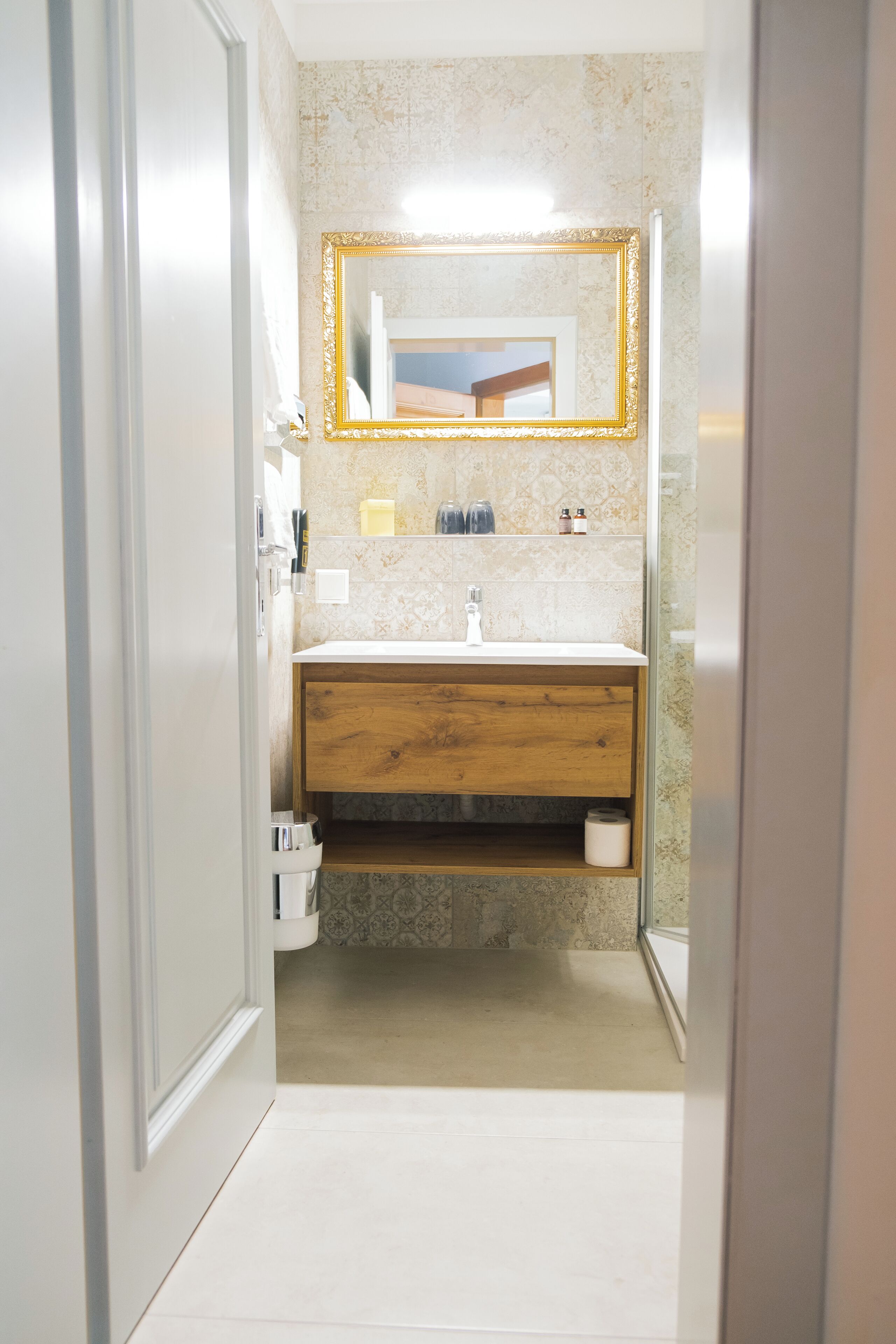 Un baño estrecho con tocador de madera, un espejo con marco dorado y suelo de baldosas.