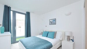 Una habitación de hotel moderna con una cama, una mesita de noche, una lámpara y un ventanal con cortinas.