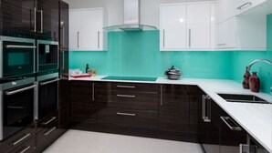 Una cocina moderna con armarios oscuros, encimera blanca y salpicadero color turquesa.