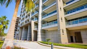 A multi-story hotel with balconies, a central entrance, and palm trees in the foreground. - Charming apartment in Sport city (Dubai)
