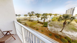 A balcony with a view of a landscaped area, palm trees, and a beach.