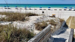 Una spiaggia con sabbia bianca, ombrelloni azzurri e lettini.