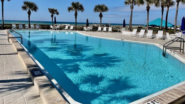 Una piscina con acqua cristallina azzurra, circondata da palme e lettini.
