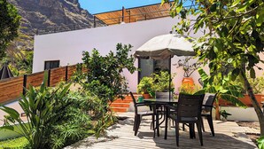 Une terrasse avec une table et des chaises, entourée de plantes en pot et d’une plateforme en bois.