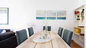 Un coin repas avec une table en bois, des chaises, un plateau contenant de la verrerie et une bibliothèque remplie de livres et d’objets décoratifs.