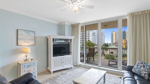 Ein Wohnzimmer mit einer Couch, einem Fernsehschrank, einem Deckenventilator und einem großen Fenster mit Blick auf Gebäude.