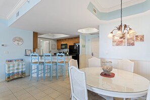 Une cuisine moderne avec des meubles en bois, un réfrigérateur noir et un four à micro-ondes. On y trouve un coin repas avec une table et des chaises blanches, et un lustre au-dessus.