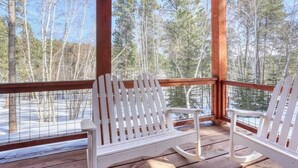 A wooden deck with two white Adirondack chairs facing a snowy landscape and a forest. - Stem Winder Lodge - Wifi, A/C, Hot tub (Lead)