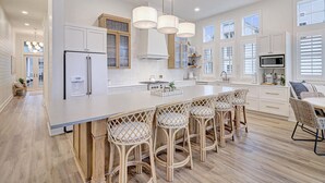 A modern kitchen with a large island, bar stools, and a dining area. - Special Lakeside Home @ Cinnamon Shore South w/Access to On-Site Amenities (Port Aransas)