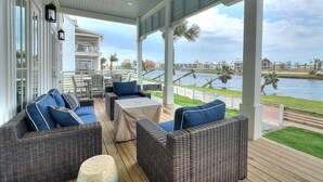 A covered outdoor seating area with wicker furniture and a view of the water. - Special Lakeside Home @ Cinnamon Shore South w/Access to On-Site Amenities (Port Aransas)