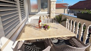 A balcony with a table set for two, featuring a bottle of wine, glasses, and grapes. - Easy City Access: 3BR w/ Balcony & Private Carport (Zadar)