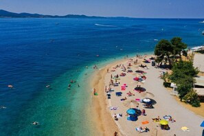 A beach with clear blue water, people swimming and sunbathing, and umbrellas on the sand.