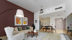 Ein modernes Wohnzimmer mit Sofa, Sessel und Couchtisch, ein Essbereich mit Stühlen und Tisch sowie eine Küche im Hintergrund.