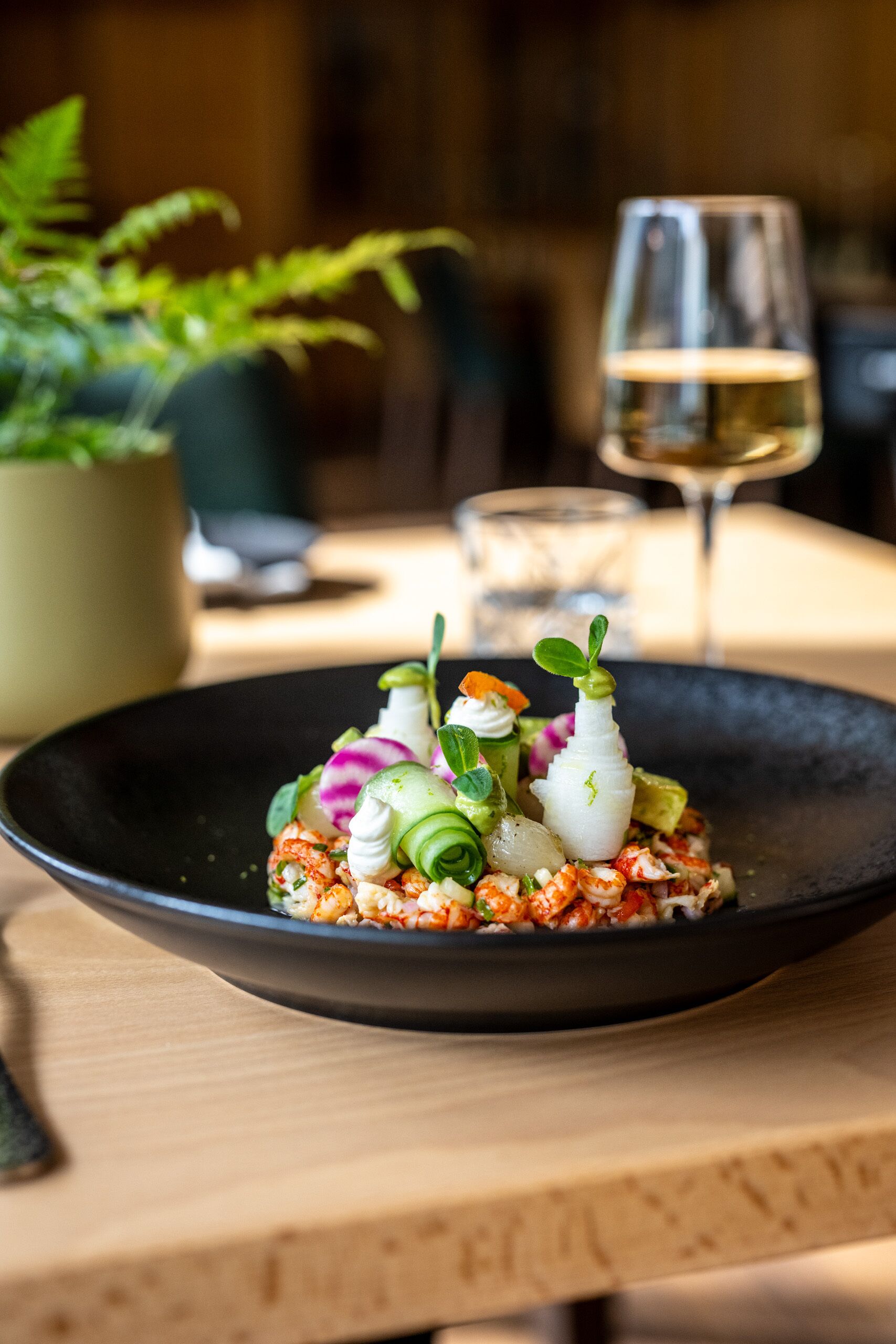 Une assiette noire sur laquelle est servi un plat de fruits de mer, le tout posé sur une table en bois.