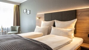 A hotel room with a large bed, a bedside table, a chair, and a view of the city. - Uferdeck - Boutique Hotel (Traben-Trarbach)