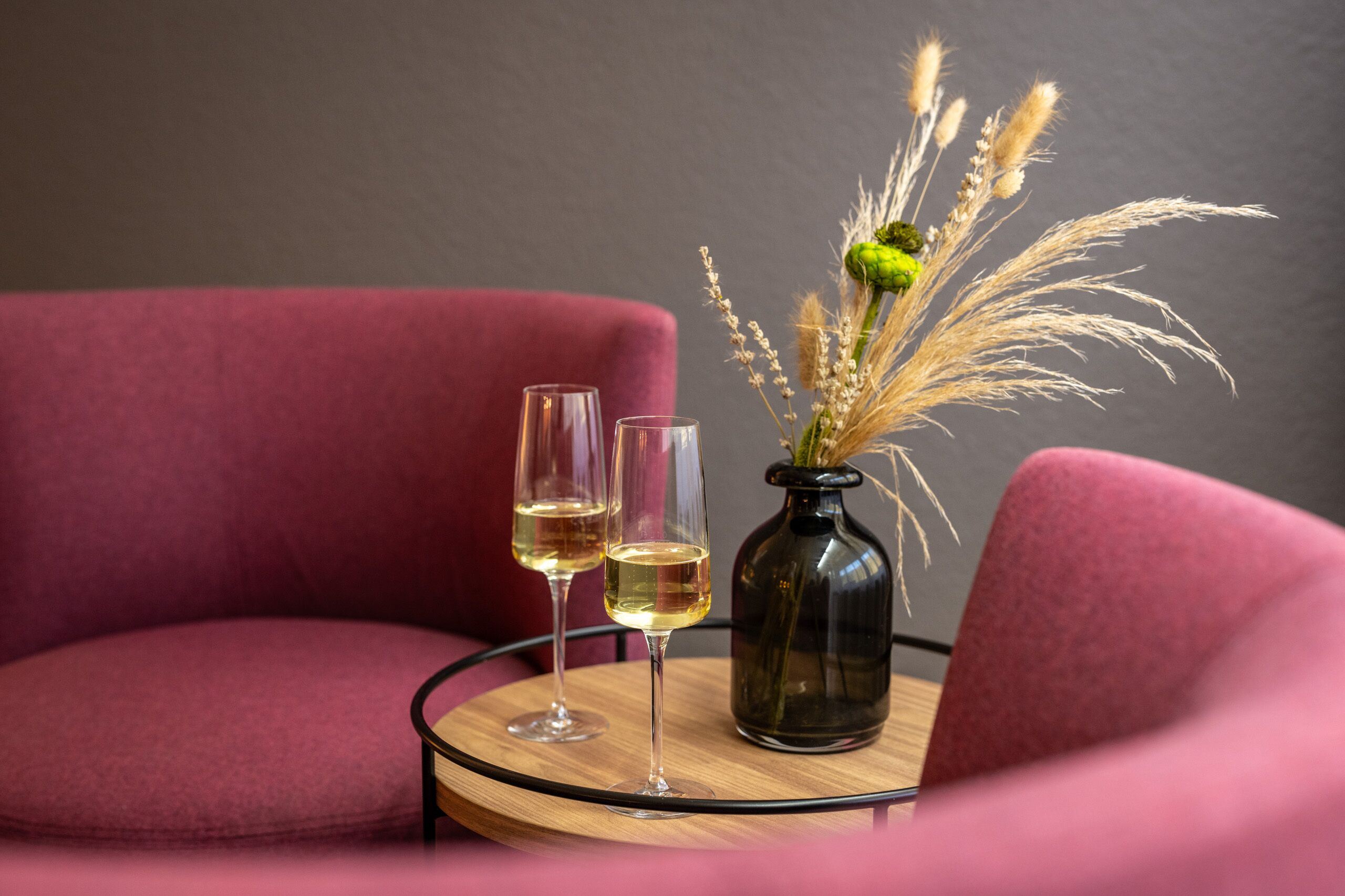Dos copas de vino blanco sobre una mesa redonda con un florero de plantas secas.