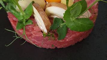 Un plato de tartare de res con huevo, champiñones y vegetales verdes sobre un plato negro.