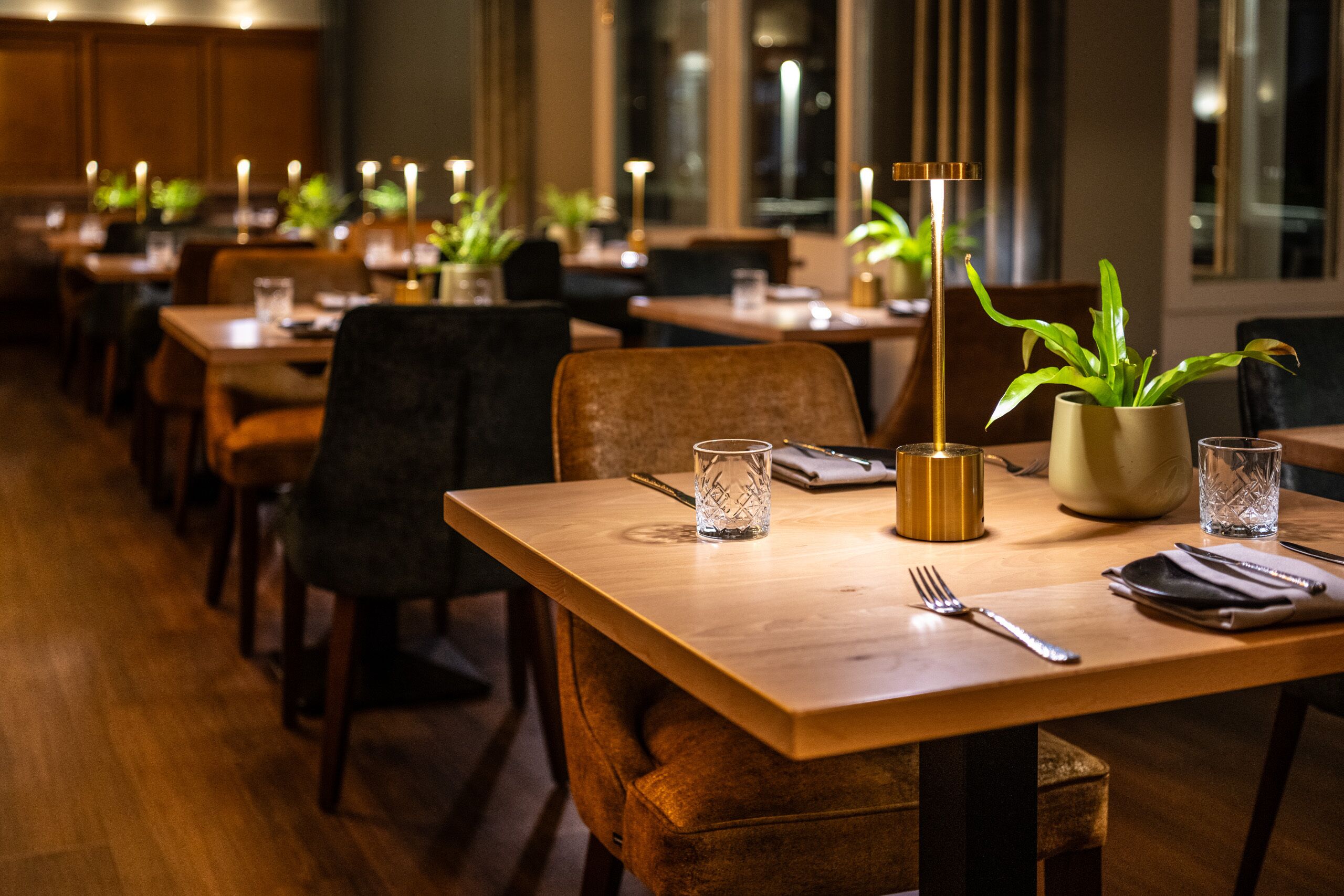 Un restaurante con mesas y sillas de madera, velas y plantas en macetas.