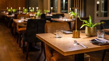 Un restaurante con mesas y sillas de madera, velas y plantas en macetas.