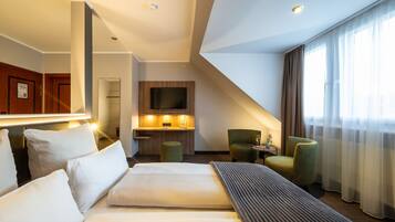 Habitación de hotel con una cama grande, un escritorio con televisor de pantalla plana, un sillón verde y un ventanal con cortinas.