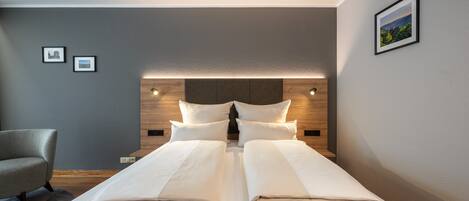 A modern hotel room with a large bed, a wooden headboard, and a gray wall with two framed pictures.