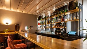 A bar area with a long counter, multiple shelves stocked with bottles, and several cushioned bar stools. - Uferdeck - Boutique Hotel (Traben-Trarbach)