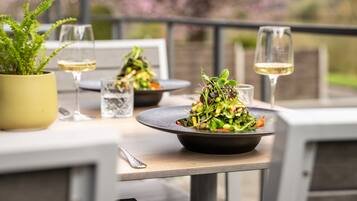 A dining table with a black bowl of salad, a glass of white wine, and a potted plant.