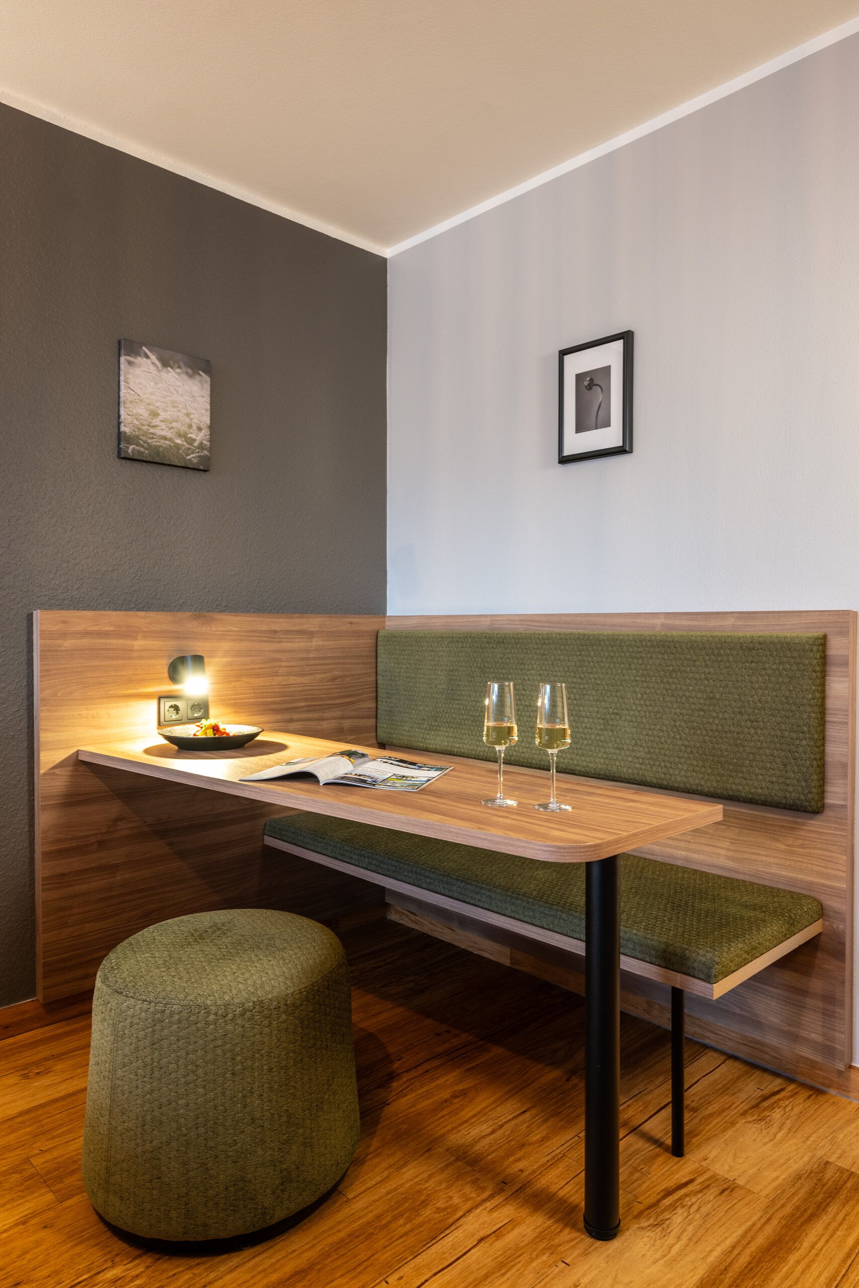 Een moderne eetruimte met een houten tafel, een groene gestoffeerde bank en een klein rond voetenbankje.