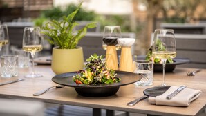 A dining table with a black bowl of salad, wine glasses, cutlery, and a potted plant. - Uferdeck - Boutique Hotel (Traben-Trarbach)