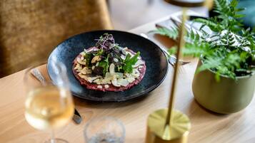 A dining table with a black plate of food, a glass of white wine, and a potted plant.