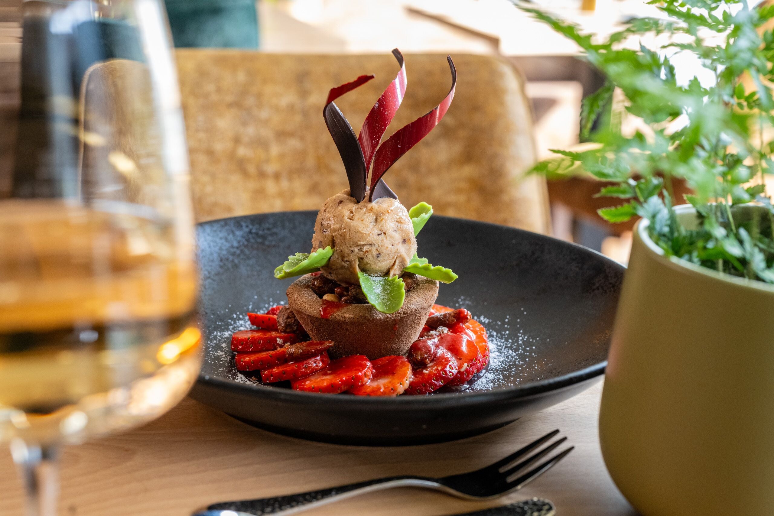 A plate with a food item, a glass of white wine, and a fork on a table.